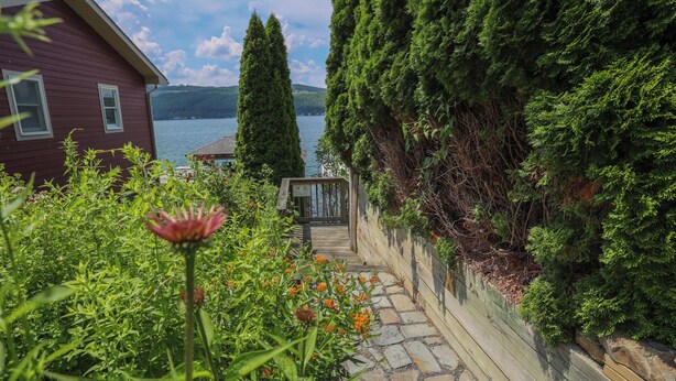 A wooden deck leading to a wooden gate, surrounded by lush greenery and a lake view.