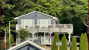 A two-story house with a balcony, a dock with chairs, and a boat.