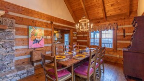 Un comedor rústico de madera con pared de piedra, vigas de madera en el techo y una araña.