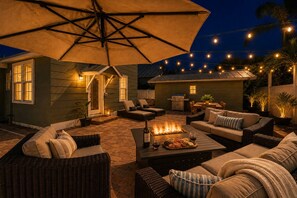 An outdoor patio area with a fire pit, seating, and string lights.