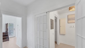 A hallway with white walls and doors, a wooden staircase, and a hanging light fixture.