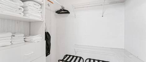 A white closet with shelves for folded clothes and a hanging rack for a jacket.