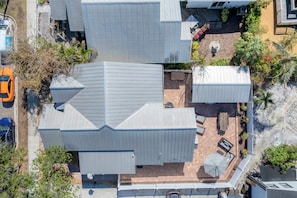An aerial view of a modern house with a sloped roof, a patio with outdoor furniture, and a small garden area.