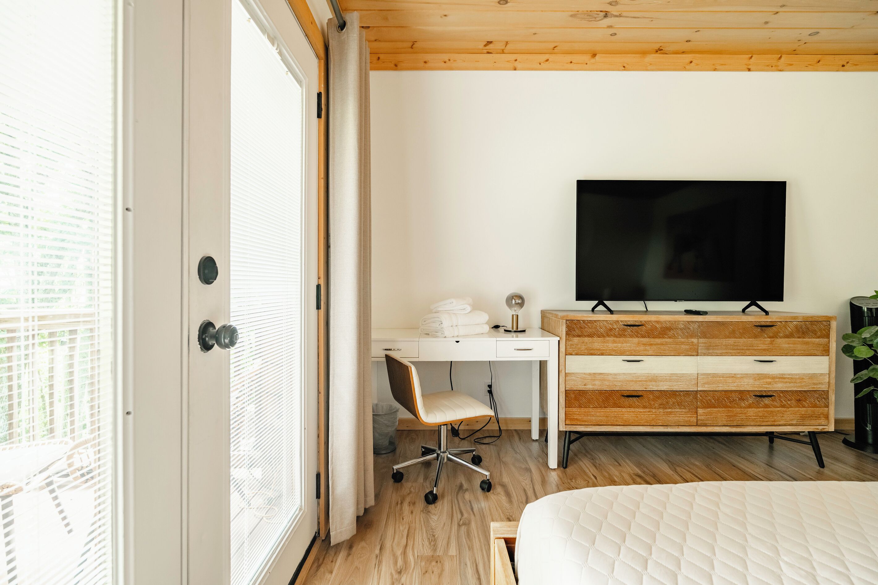 A bedroom with a bed, a desk, a TV, and a dresser.