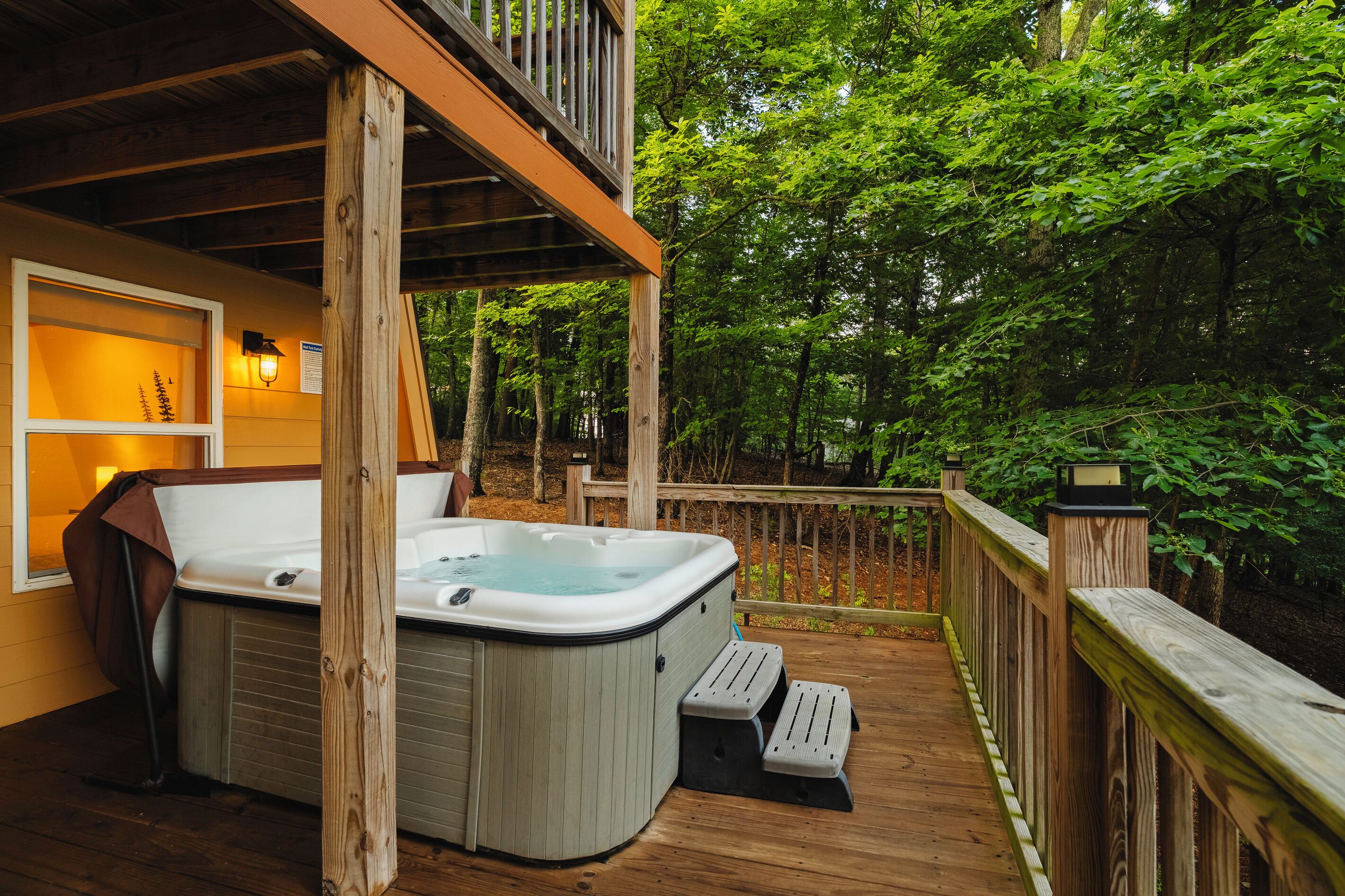 Un jacuzzi en una terraza de madera con baranda, rodeado de árboles.