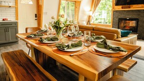 Ein Essbereich mit Holztisch, gedeckt für vier Personen, einem Kamin und Blick auf Bäume durch große Fenster.