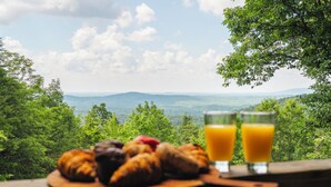 Frühstückstisch mit Croissants, Muffins und Orangensaft, mit Blick auf eine schöne Landschaft.
