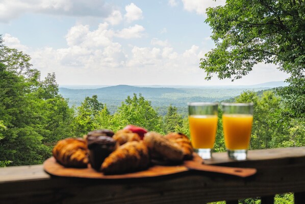 A breakfast setting with croissants, muffins, and orange juice on a wooden table with a scenic view.