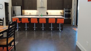 A modern kitchen with dark cabinets, a central island with bar stools, stainless steel appliances, and pendant lighting. - Red Rock Oasis and Private Pool Getaway! (Moab)