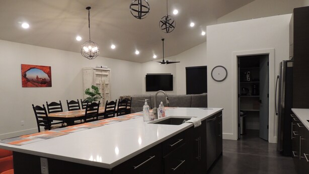 A modern kitchen with a large island, dark cabinetry, and pendant lighting. - Red Rock Oasis and Private Pool Getaway! (Moab)