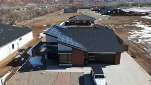 A modern building with solar panels on the roof, a driveway, and a mountainous backdrop. - Red Rock Oasis and Private Pool Getaway! (Moab)