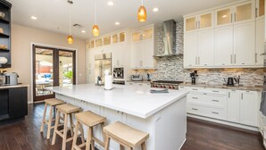 A modern kitchen with white cabinets, a large island with stools, stainless steel appliances, and pendant lighting. - Hidden Gem of SoCal: Game Room, Pool, Spa, & Resort Backyard!  (Vista)