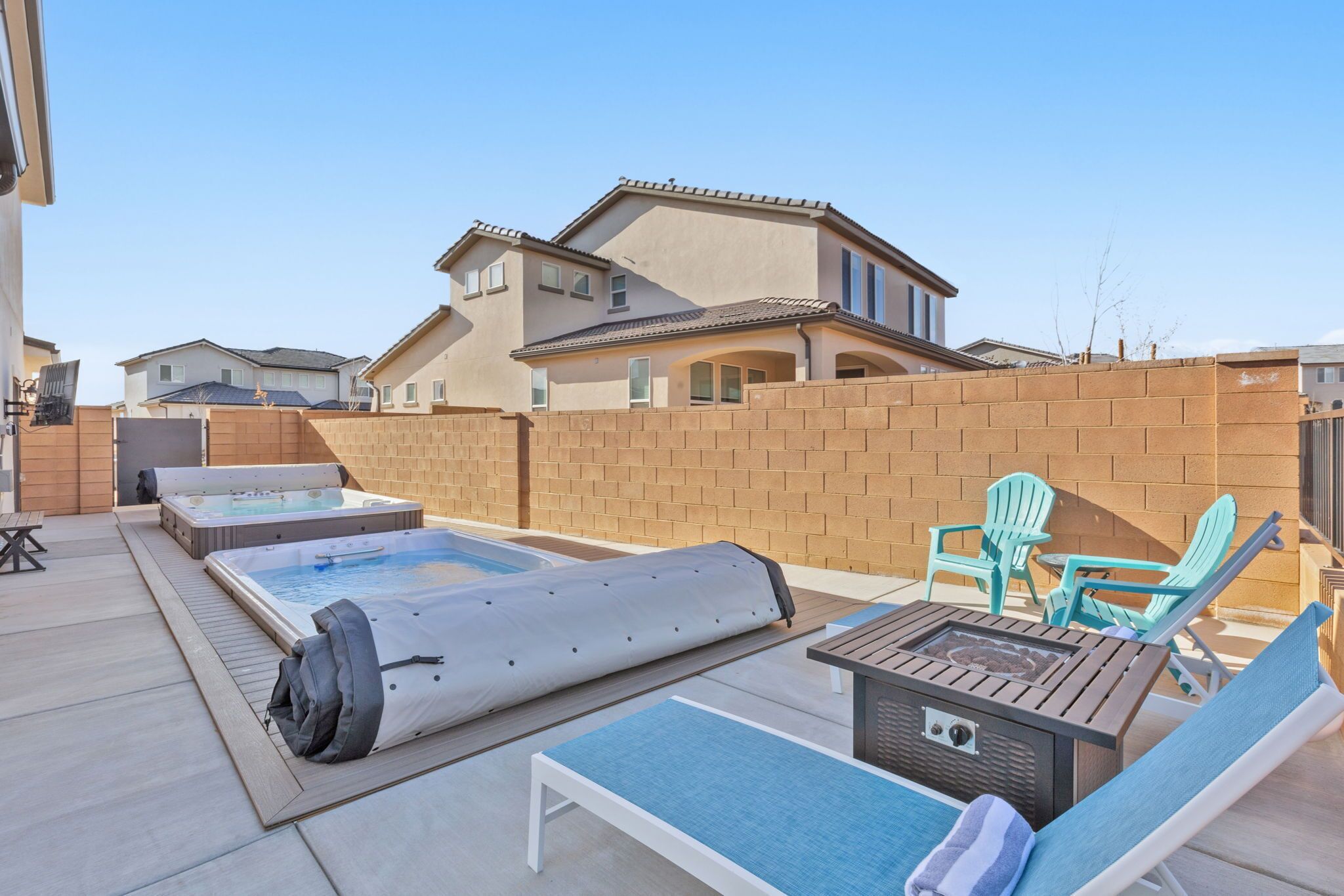 A backyard with a hot tub, lounge chairs, and a barbecue grill.