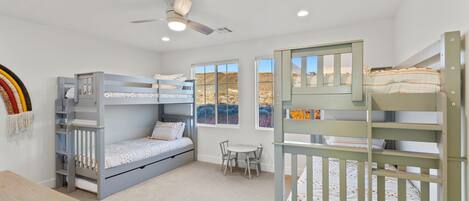 Une chambre d’enfant avec des lits superposés, un bureau et un ventilateur de plafond.
