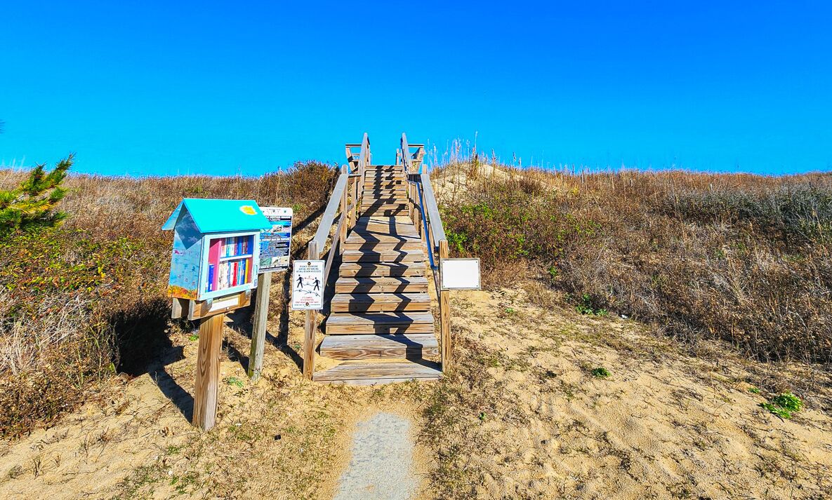 Una escalera de madera que lleva a una zona de playa con una pequeña estructura a la izquierda.