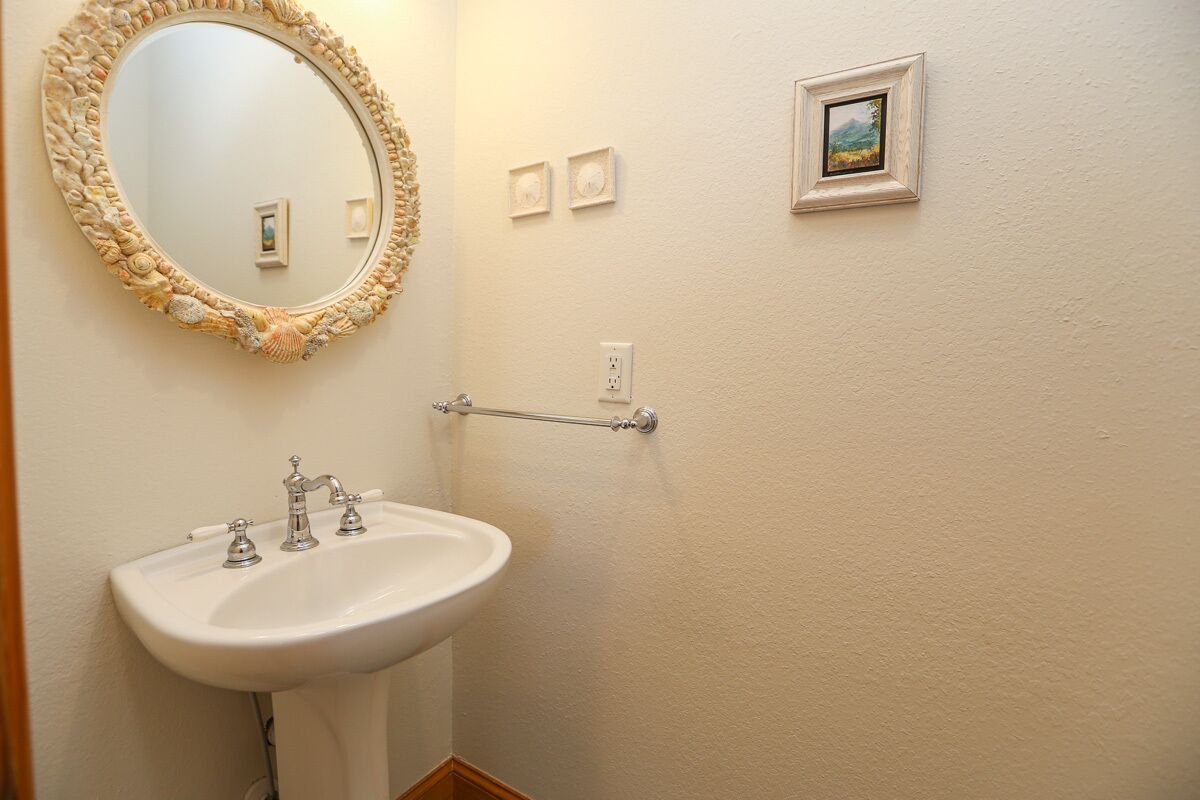 A bathroom with a white sink, a round mirror with a seashell frame, and a towel rack.