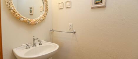 A bathroom with a white sink, a round mirror with a seashell frame, and a towel rack.