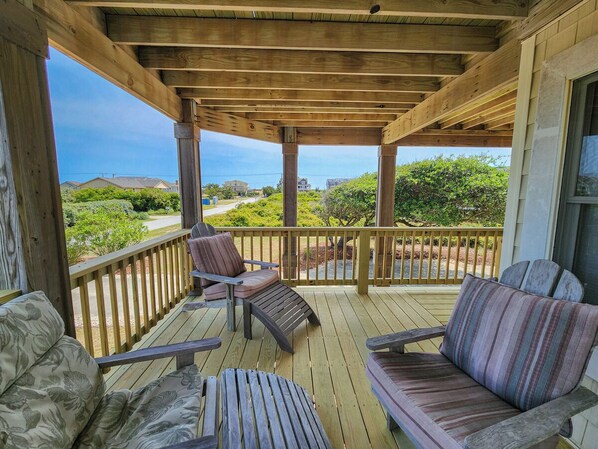A covered outdoor deck with wooden furniture, including two chairs and a sofa, overlooking a residential area.