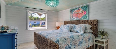 A bedroom with a bed, a window, a wall-mounted artwork, and a bedside table.