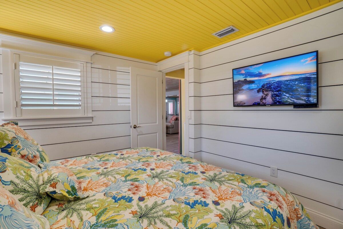 A bedroom with a bed, a television on the wall, and a window with blinds.