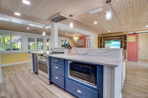 A modern kitchen with a large island, built-in oven, microwave, and a television.