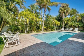 A swimming pool with lounge chairs, surrounded by palm trees.