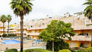 Un hôtel à plusieurs étages doté d’une piscine, de palmiers et d’un jardin bien entretenu.