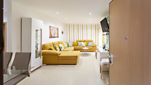 Un salon moderne avec un canapé jaune, une table basse en verre et un téléviseur posé sur un meuble en bois.