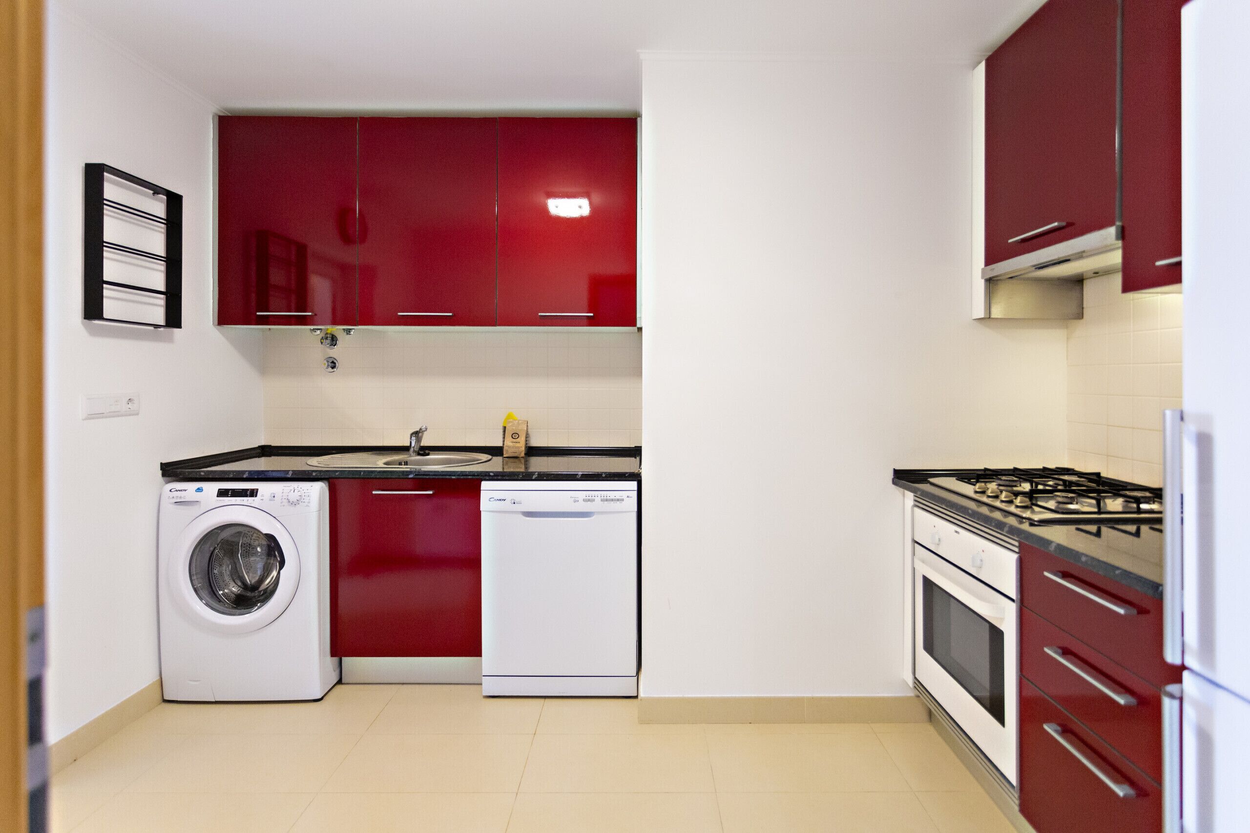 Une cuisine de taille réduite avec des meubles rouges, un lave-linge, un lave-vaisselle et une cuisinière.