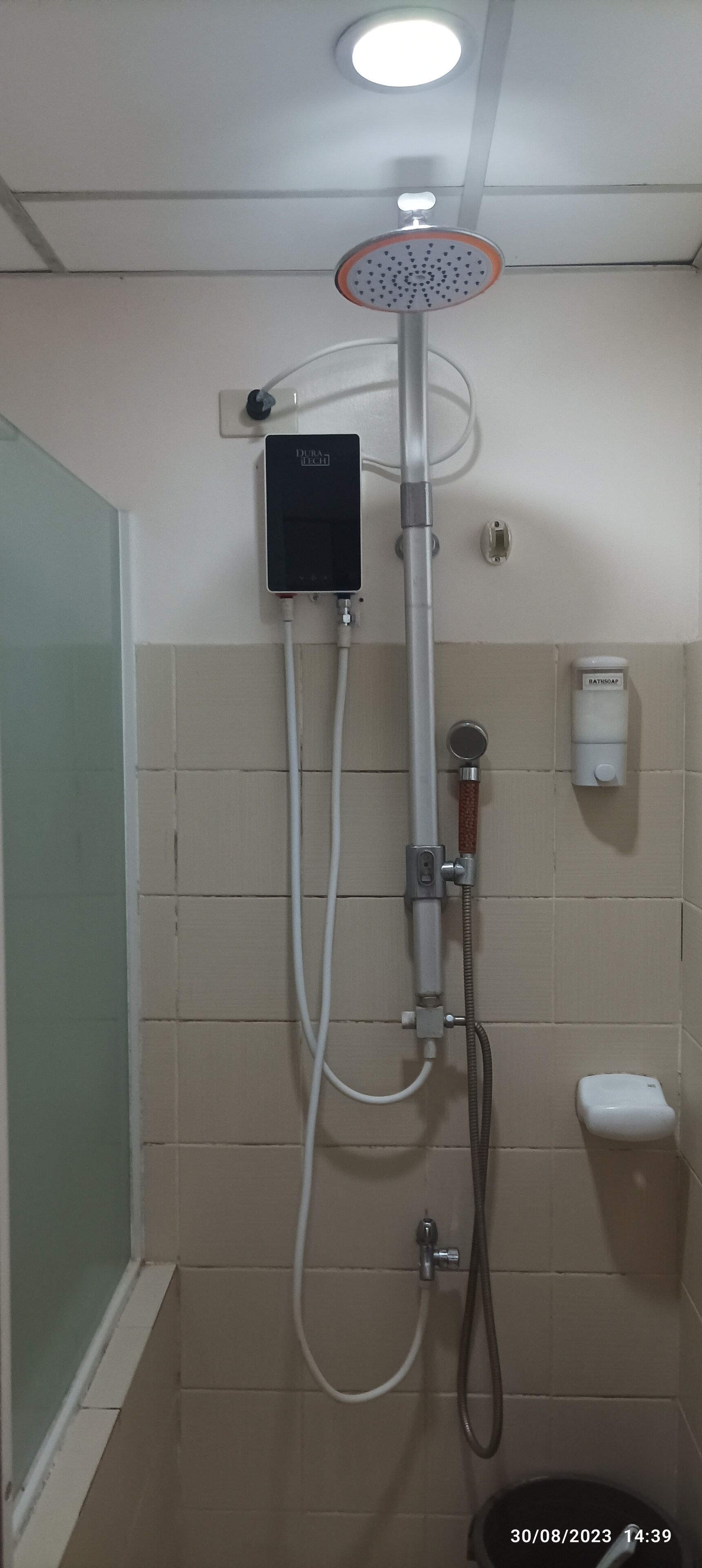 A shower with a handheld showerhead, a wall-mounted control panel, and a handheld shower attachment.