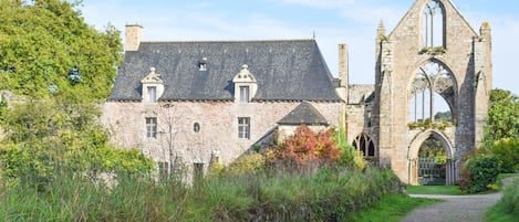 A historic stone building with a large arched entrance, a pathway leading to it, and surrounding greenery.
