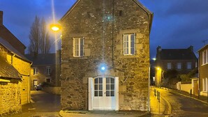 A stone building with a white door and two windows, illuminated by street lamps.