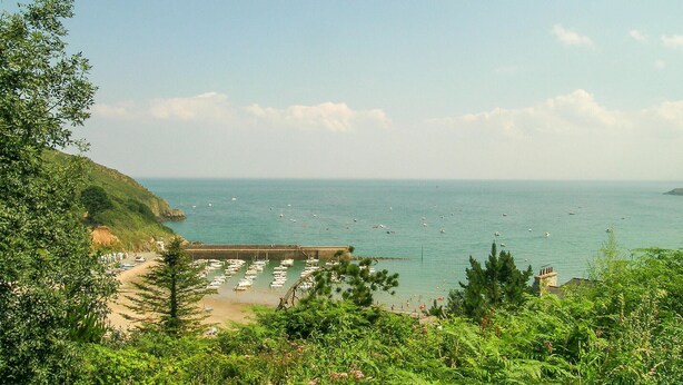 A coastal view with a beach, boats, and a rocky cliff.