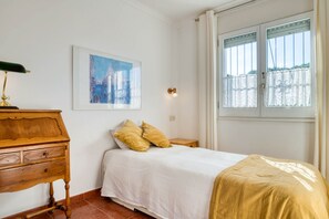 A bedroom with a bed, a wooden dresser, a framed painting, and a window with curtains.