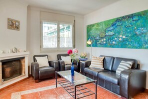 A living room with a fireplace, leather sofas, a glass coffee table, and a large painting on the wall.