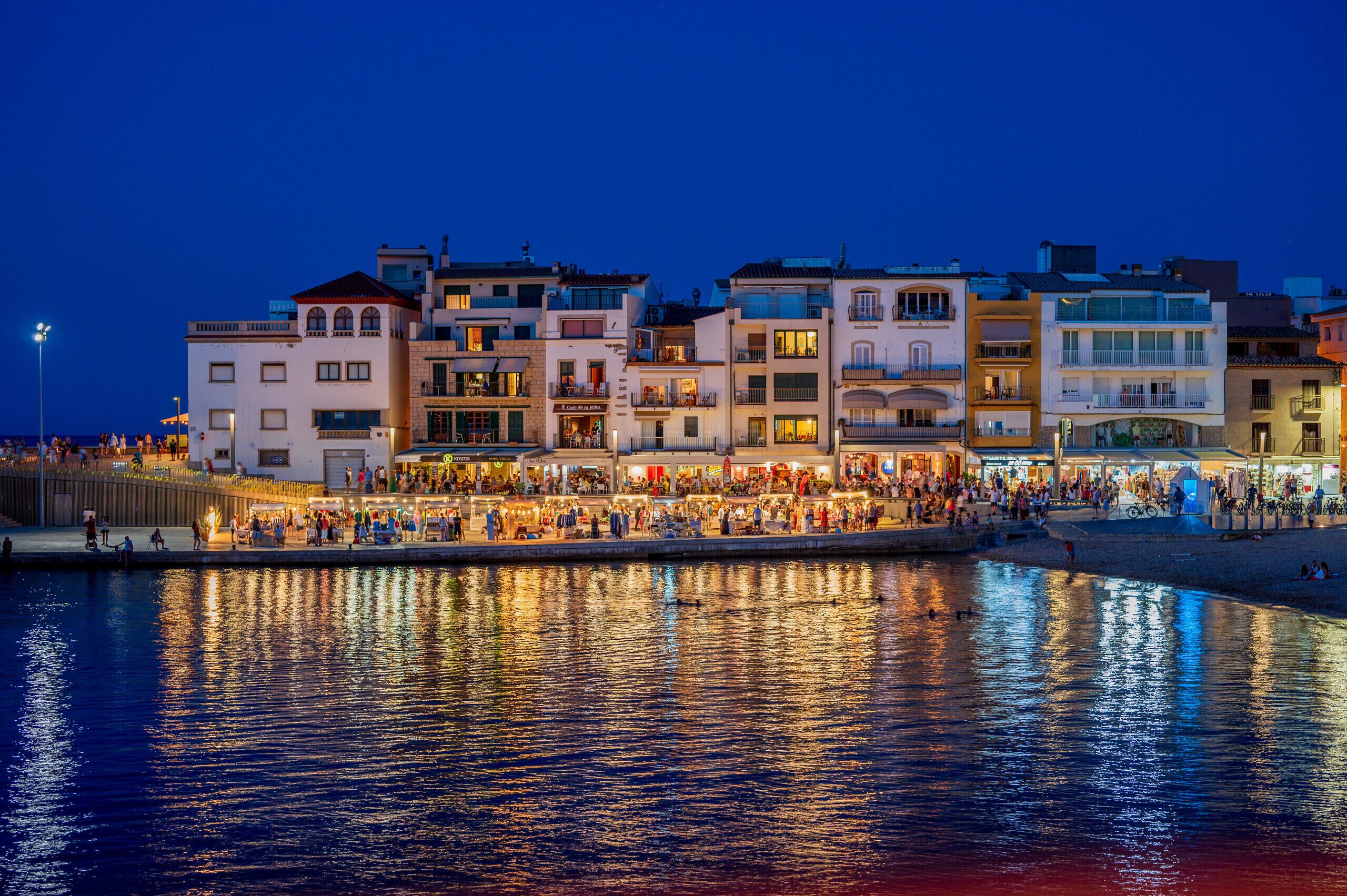 A waterfront promenade with buildings, shops, and people.