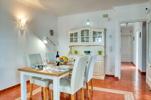 A dining area with a wooden table set for four, white chairs, and a white cabinet with glass doors.