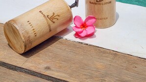 Two bamboo lotion bottles with a pump dispenser and a pink flower on a wooden surface by a pool. - Bamboo Lodge Private Villa (Gili Trawangan)