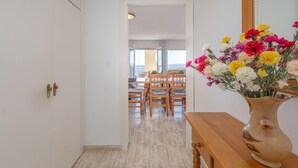 A hallway leading to a dining area with a wooden table and chairs, a vase of flowers on a table, and a view through an open door. - Pleasant apartment with sea view (Empuriabrava)