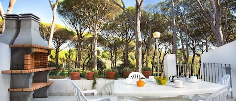Eine Terrasse im Freien mit einem Backstein-Grill, weißen Stühlen, einem Tisch und Topfpflanzen.