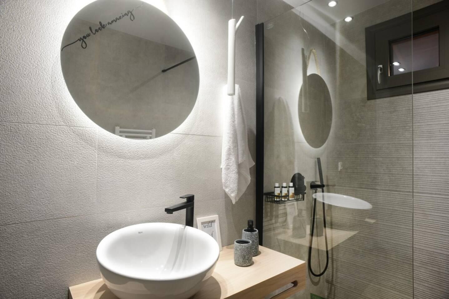 A modern bathroom with a round mirror, a white sink, and a glass shower enclosure.