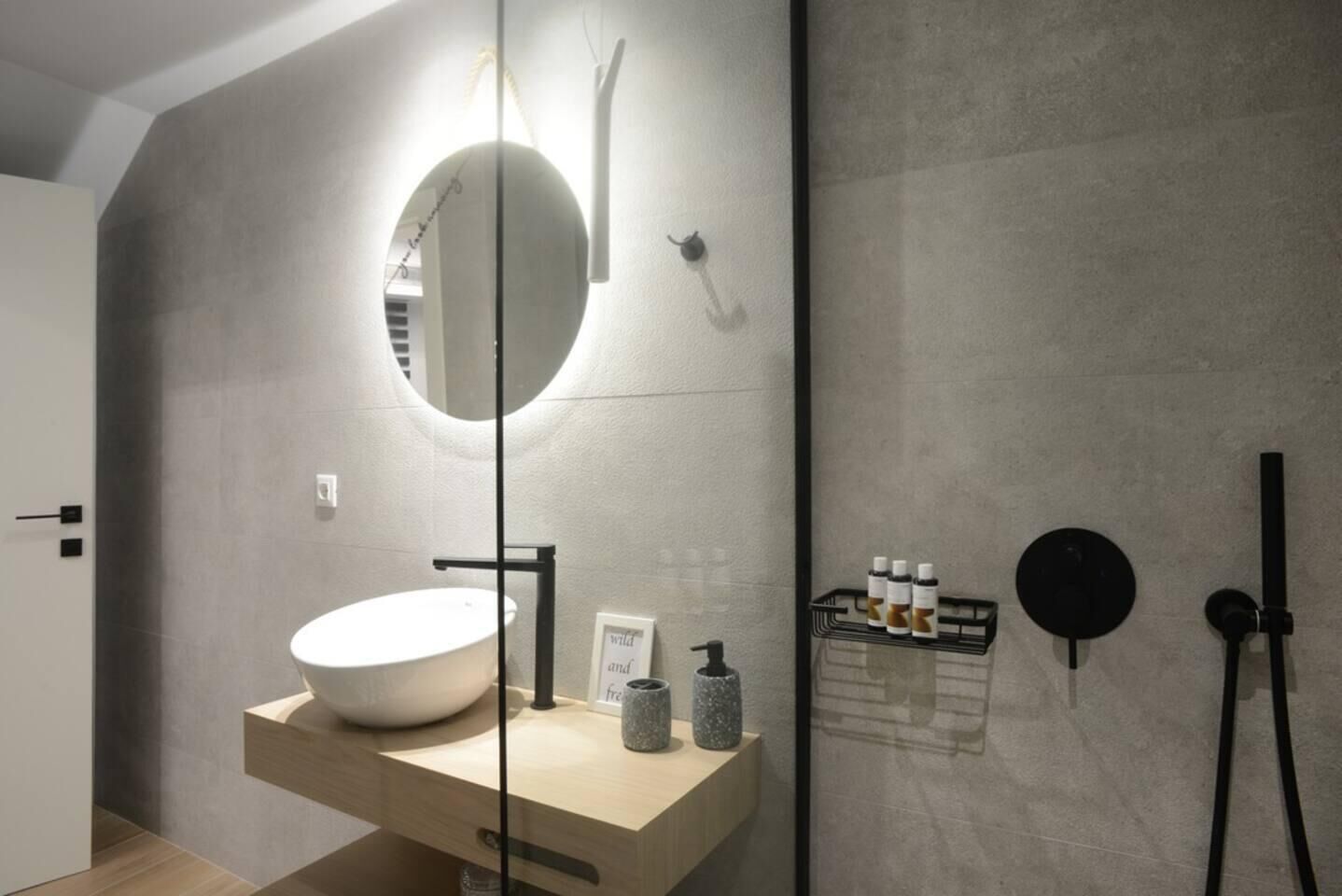 Une salle de bain moderne avec un grand lavabo ovale, un miroir rond et un espace douche.