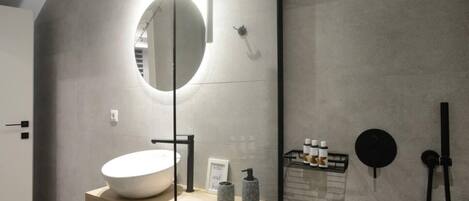Une salle de bain moderne avec un grand lavabo ovale, un miroir rond et un espace douche.