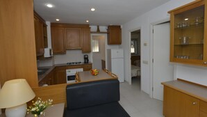 Una cocina compacta con armarios de madera, una mesa de comedor con sillas, un refrigerador y un pequeño aparador con cristalería.