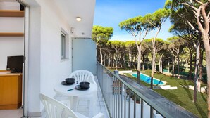 Un balcón con mesa y sillas, con vista a una piscina y árboles.