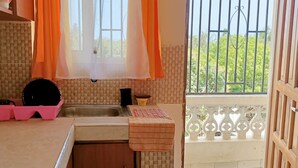 A kitchen with a sink, pink egg cartons, a black pot, and a window with orange curtains. - 2-Bed Penthouse in Mtwapa with Rooftop Terrace (Mtwapa)