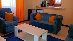 A living room with two blue armchairs, a white coffee table, and orange curtains. - 2-Bed Penthouse in Mtwapa with Rooftop Terrace (Mtwapa)