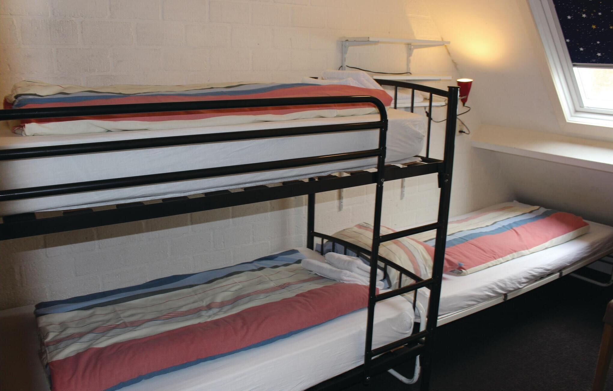 A bunk bed with three levels, white walls, a window with a starry night view, and a red cup on the nightstand.