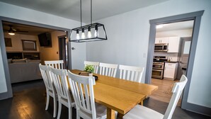 Ett modernt matområde med ett träbord och vita stolar, en hänglampa och utsikt in i köket.