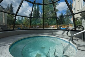 A pool area with a glass enclosure, lounge chairs, and a view of trees and a building. - Ski in/Out 2 Bed/2bath w Pool/HotTub & Great Light (Whistler)